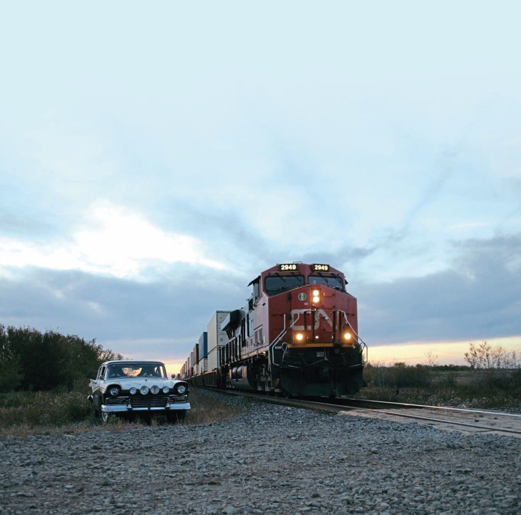 1957 Ford parked next to the train tracks as a train passes