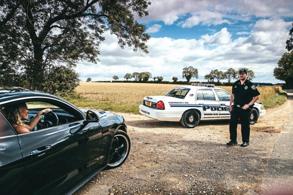 Ewan in an American police costume leaves his Crown Victoria and walks towards a woman in a black car.