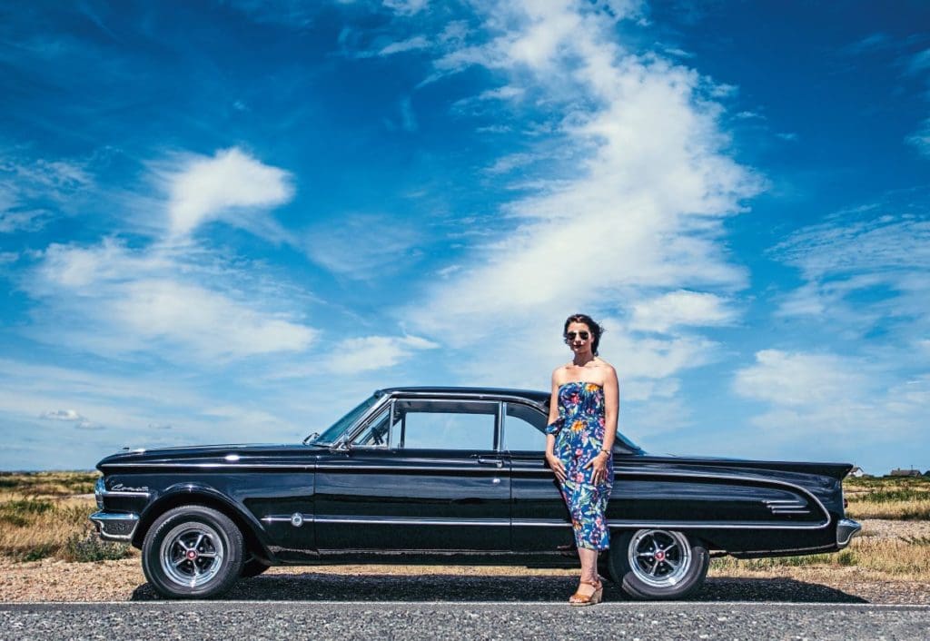 Lesley stands in front of her 1963 Mercury Comet S-22 against a blue sky