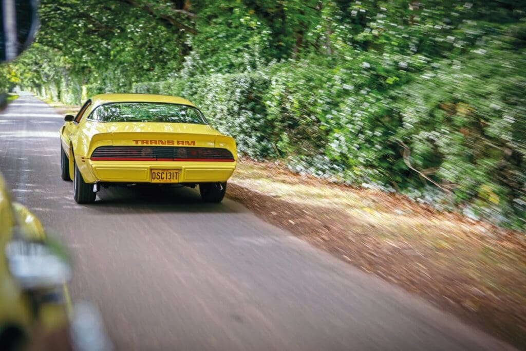 Back view of Pontiac Firebird Trans Am driving down a country road